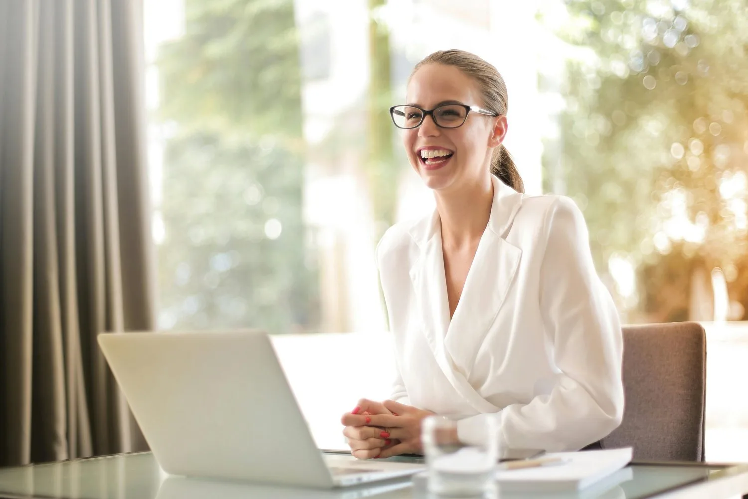 Smiling woman in a white blouse working at a laptop in a sunny office
